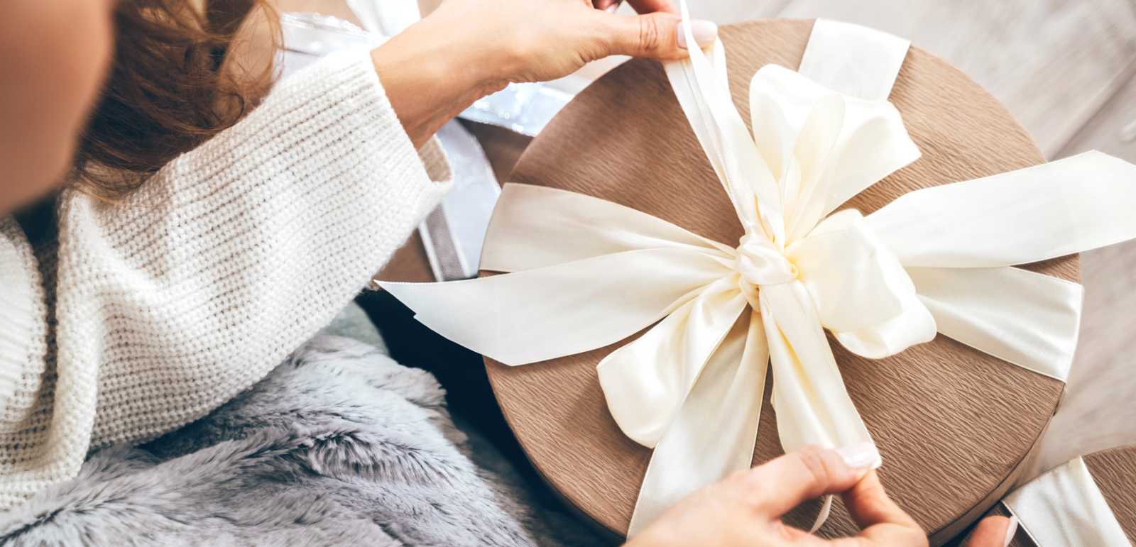 Close-up of a woman lying on soft blanket and preparing for upcoming holidays, wrapping gifts and tying a beautiful pastel ribbon bow. Black Friday sale offers concept with copy space