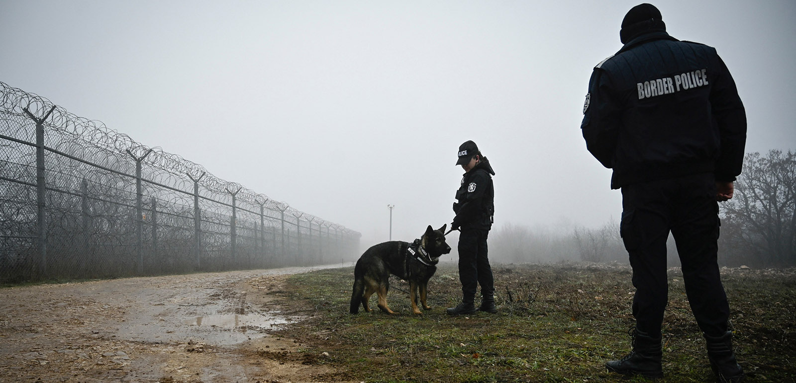 Bulgarian border police officers patrol with a dog in front of the border fence on the Bulgaria-Turkey border near the village of Lesovo on January 13, 2023. - Bulgaria faces mounting accusations that it is abusing people trying to cross its border with Turkey, with asylum seekers saying they have been pushed back, locked up, stripped and beaten. The EU member serves as a gateway into the bloc and is trying to tighten the border to stop a rising number of people seeking to cross, which has reached levels unseen since 2015. (Photo by Nikolay DOYCHINOV / AFP) (Photo by NIKOLAY DOYCHINOV/AFP via Getty Images)