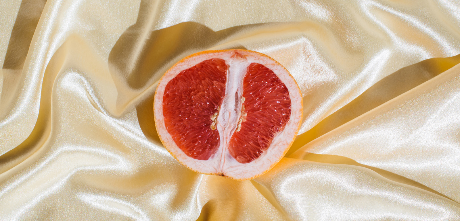 Fresh grapefruit on beige soft silk fabric background. Sex concept. Women's health, sexuality, erotic tension. Female vagina and clitoris symbol.