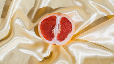 Fresh grapefruit on beige soft silk fabric background. Sex concept. Women's health, sexuality, erotic tension. Female vagina and clitoris symbol.