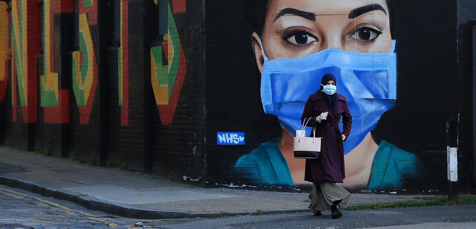 A woman wearing a face mask walks past an NHS mural during the Covid pandemic in April, 2020 in Shoreditch, London