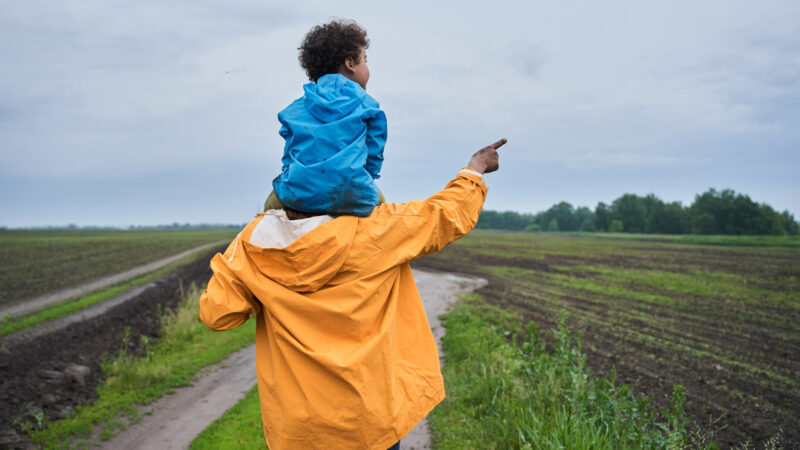 Man holding son on his shoulders while walking along a path