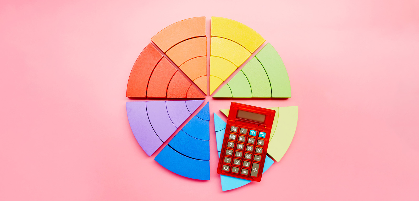 High angle view of a pie chart made of colorful building blocks and red calculator on pink background. Photo by Getty Images