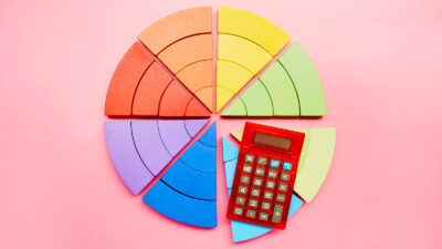 High angle view of a pie chart made of colorful building blocks and red calculator on pink background. Photo by Getty Images. Photo used to illustrate muslim rotating savings banks ajo ayuutokameti pardner adashi