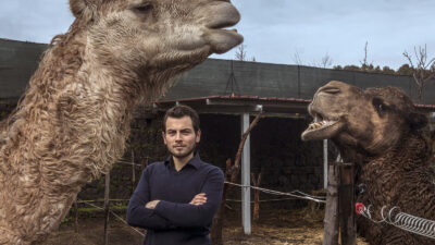 A man stands beside two camels, posing for a photo.
