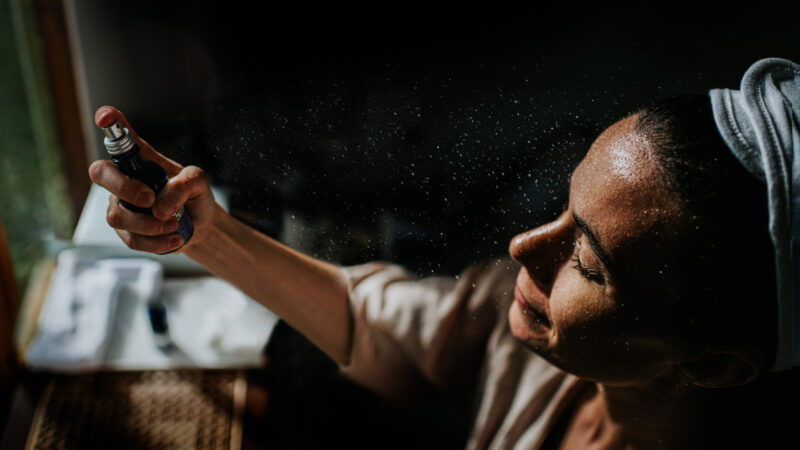 A woman sprays a skin care product on to her face.