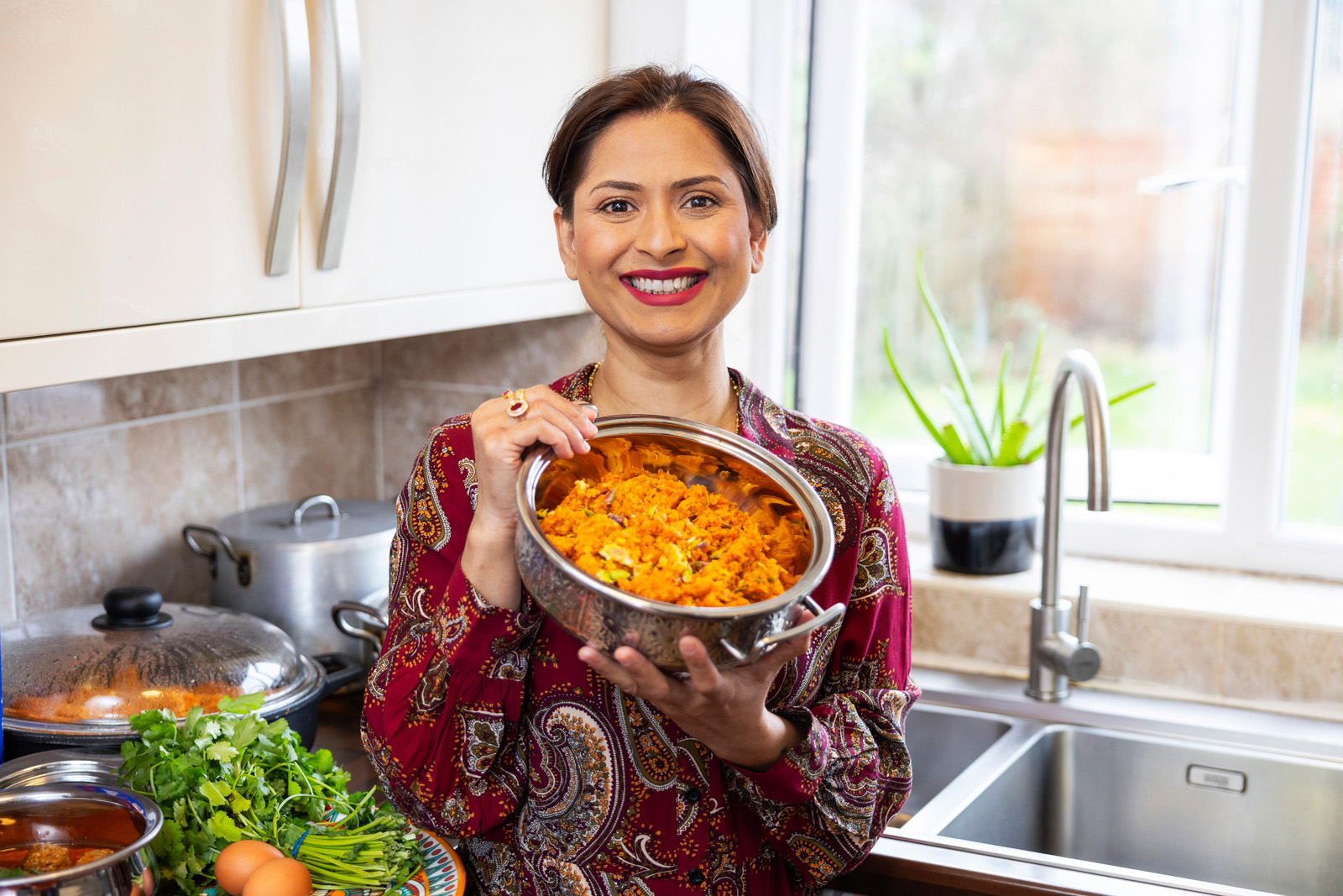Rameen Kay stands in her kitchen, holding up a pan containing pulao.