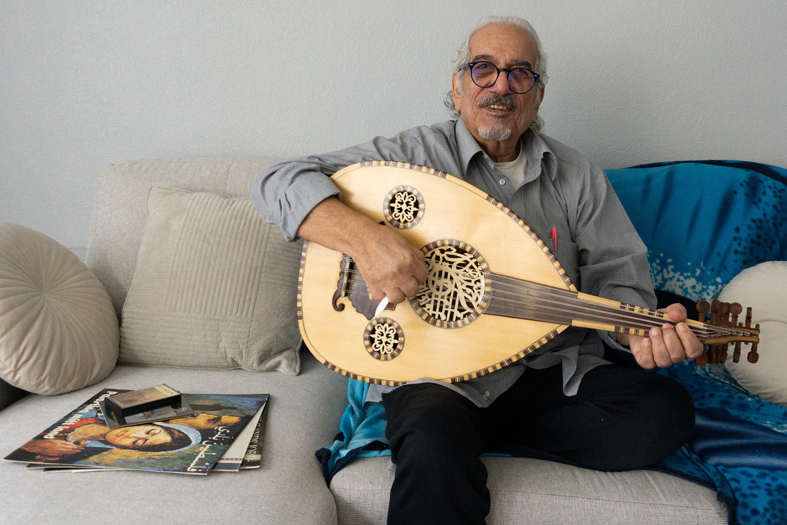 Musician George Totari plays the oud instrument on a couch.