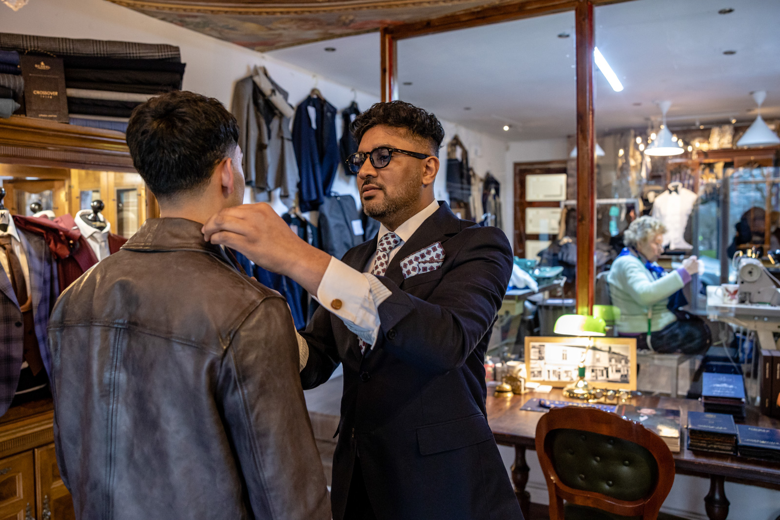 A tailor inspects the collar of a client's leather jacket.