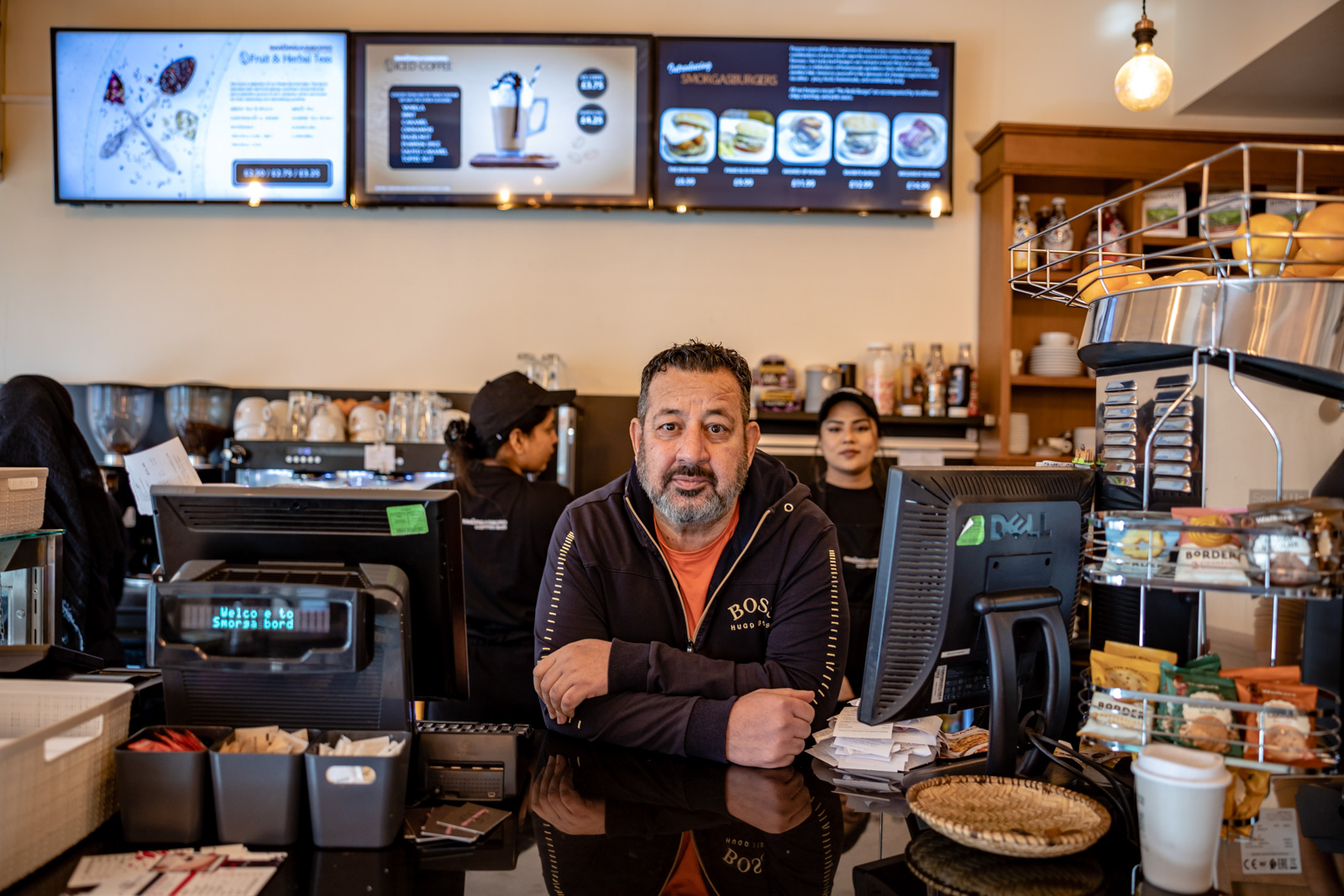 A cafe owner poses for a photo behind the till.