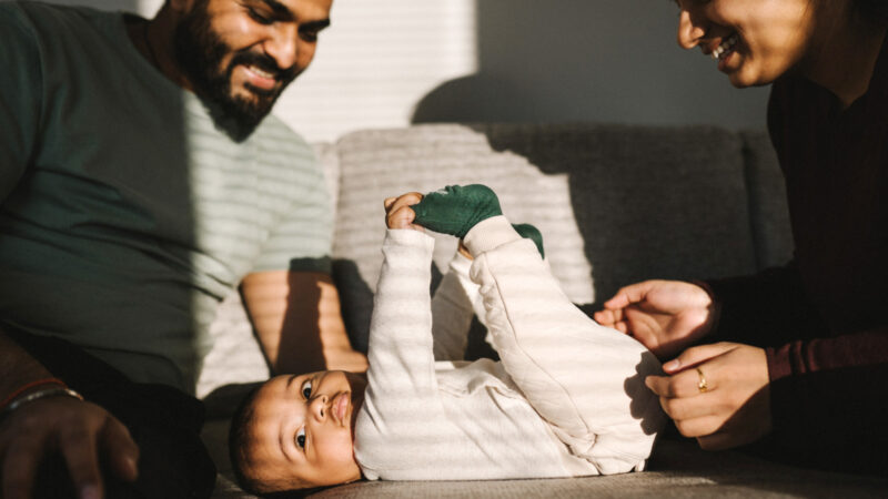 A couple plays with their infant on a sofa.