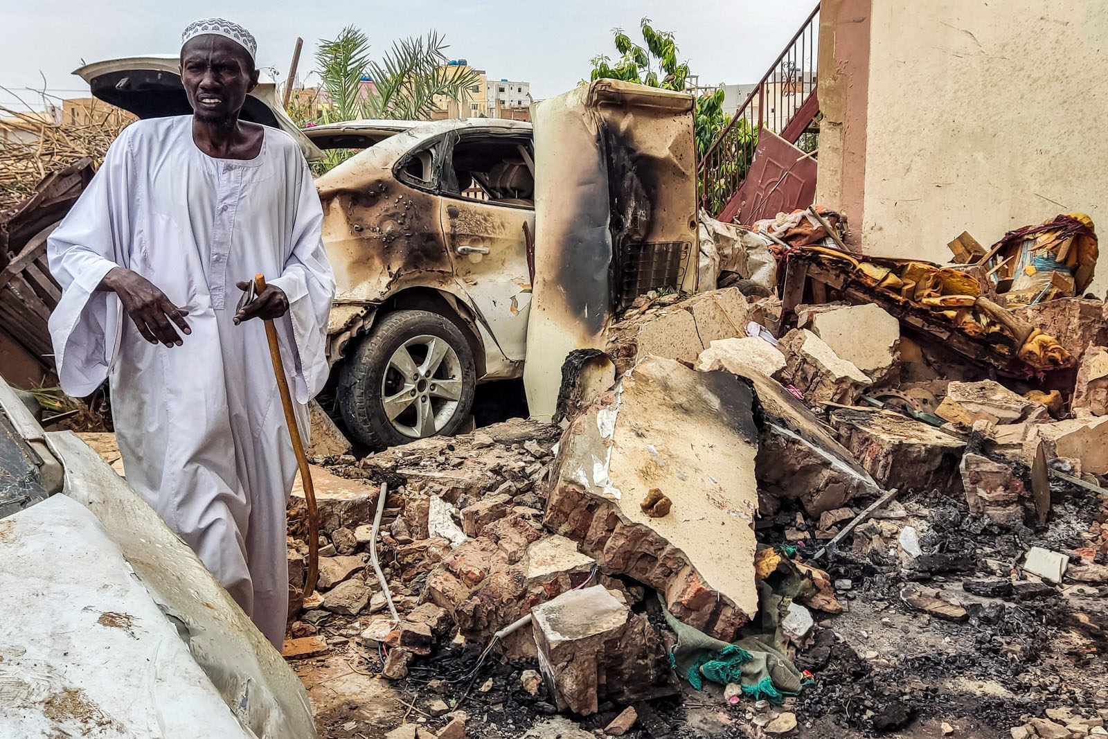 A man inspects damage as he walks through the rubble by a destroyed car outside a house that was hit by an artillery shell in the Azhari district in the south of Khartoum.