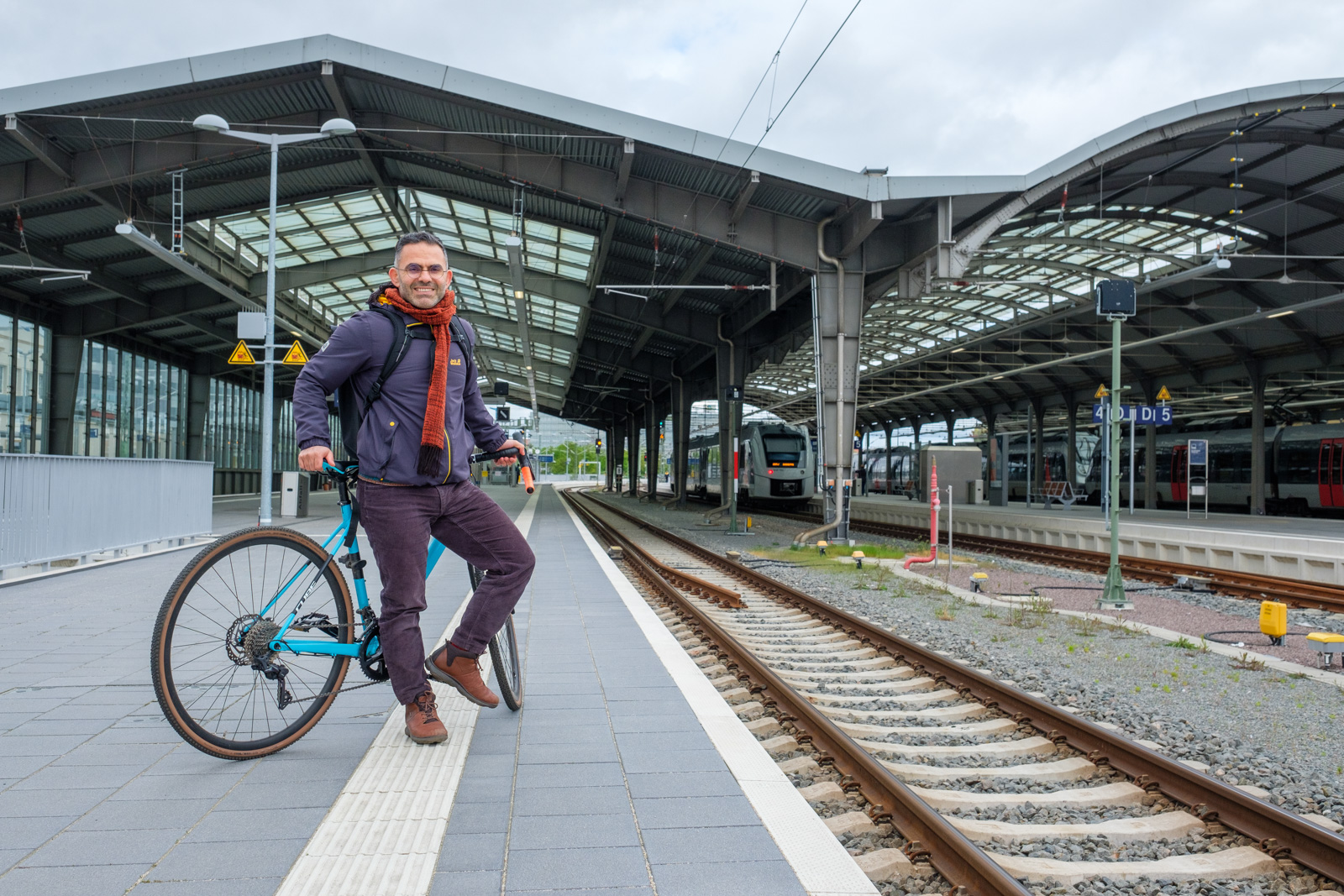 A man on his bike waits for a train on a station platform.