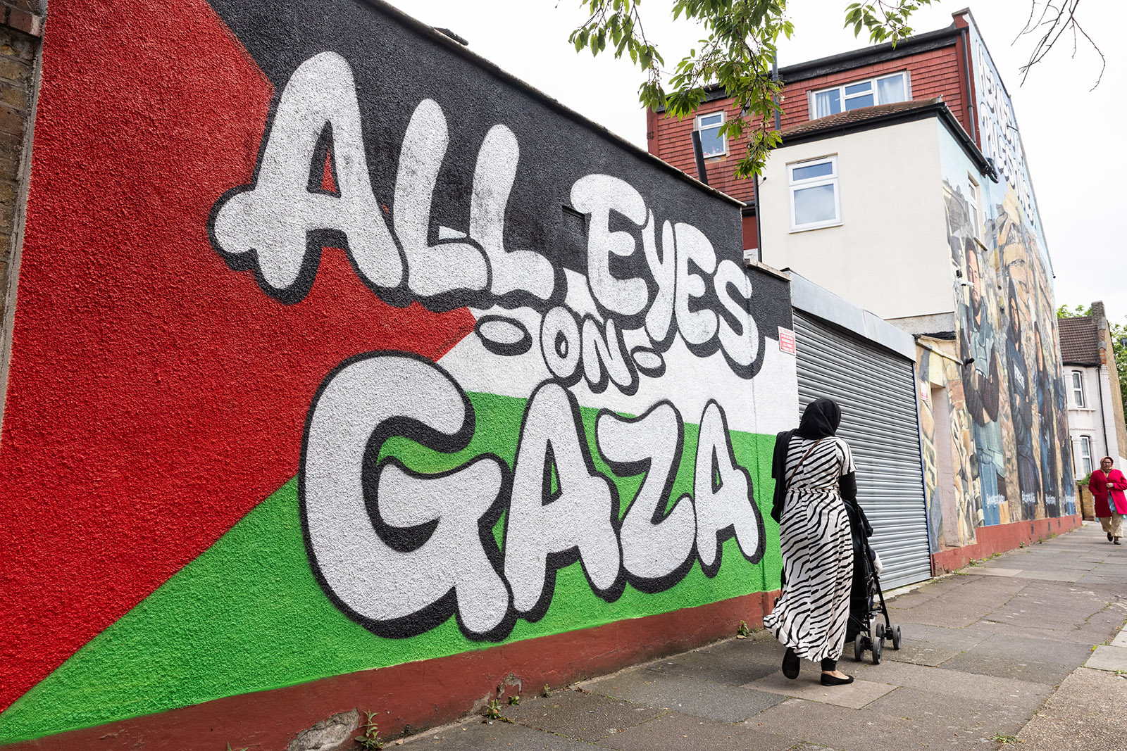 Members of the public pass pro-Palestinian street art in tribute to Palestinian journalists Mohamed Al Masri, Ali Jadallah, Hind Khoudary and Abdulhakim Abu Riash in Ilford on 7th May 2024 in London, United Kingdom. The artwork, which is in two sections, consists of the words 'All Eyes On Gaza' on a Palestinian flag and a painted rendering of a photograph of the four journalists with the words 'Heroes of Palestine' above. It was produced by Creative Debuts, an art platform providing opportunities and support to emerging artists from around the world. (photo by Mark Kerrison/In Pictures via Getty Images)