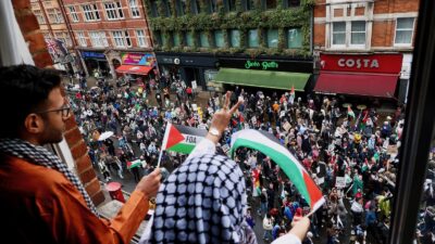 A local resident waves from her window as a pro-Palestinian demonstration passes on the road below in London, Britain July 6, 2024. Photography by Yann Tessier/Reuters