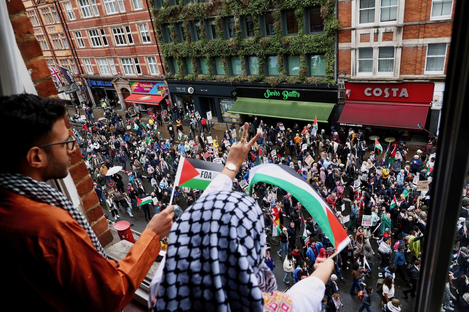 A local resident waves from her window as a pro-Palestinian demonstration passes on the road below in London, Britain July 6, 2024. Photography by Yann Tessier/Reuters