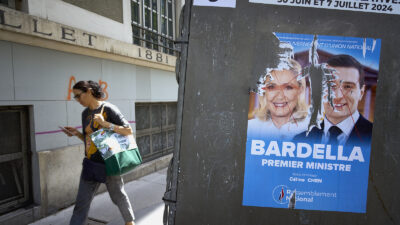 A woman passes a voting station with the electoral poster featuring the defaced photos of Marine le Pen and Jordan Bardella, of the far right party the Rassemblement National, or National Rally in the 10th arrondissement on June 23, 2024 in Paris, France. Posters with images of the candidates for the legislative elections are being put up in front of various voting stations, such as public schools and other municipality buildings. The first round of voting will take place on June 30th 2024, followed a week later by the second round of voting on July 7th 2024. These elections are the result of the decision of the French president, Emmanuel Macron, to dissolve parliament after gains by the far-right party Rassemblement National, or National Rally during the recent European elections. Photo by Remon Haazen/Getty Images