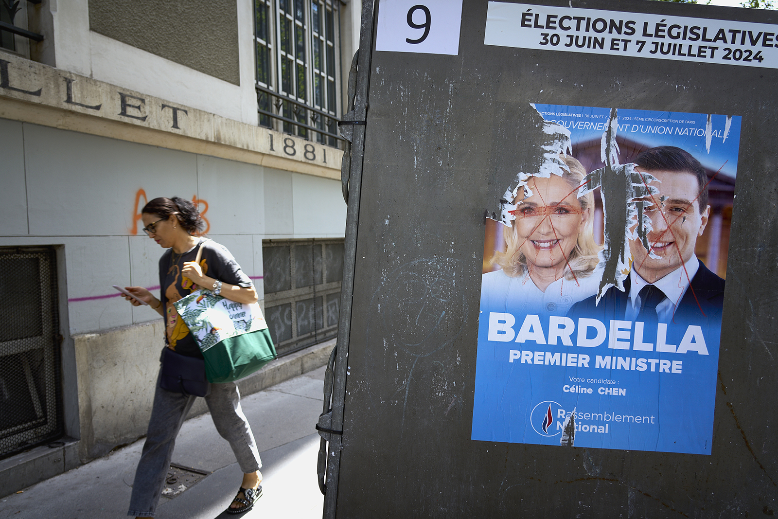 A woman passes a voting station with the electoral poster featuring the defaced photos of Marine le Pen and Jordan Bardella, of the far right party the Rassemblement National, or National Rally in the 10th arrondissement on June 23, 2024 in Paris, France. Posters with images of the candidates for the legislative elections are being put up in front of various voting stations, such as public schools and other municipality buildings. The first round of voting will take place on June 30th 2024, followed a week later by the second round of voting on July 7th 2024. These elections are the result of the decision of the French president, Emmanuel Macron, to dissolve parliament after gains by the far-right party Rassemblement National, or National Rally during the recent European elections. Photo by Remon Haazen/Getty Images