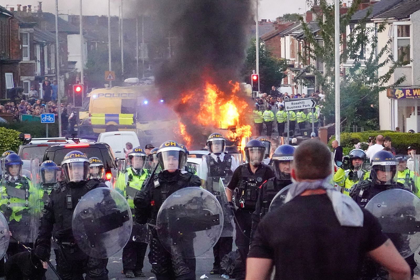 SOUTHPORT, ENGLAND - JULY 30: Riot police hold back protesters near a burning police vehicle after disorder broke out on July 30, 2024 in Southport, England. Photo by Getty Images