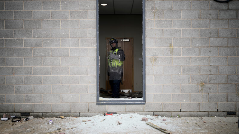 A riot police officer is seen behind a broken window in the Holiday Inn Express being used as an asylum hotel in Manvers, Rotherham on 4 August. Photo by Christopher Furlong/Getty Images