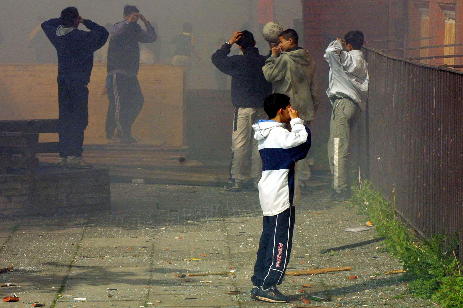 Asian children protect themselves from smoke after their football game was halted as Greenhill Mill school in the north English town of Oldham was petrol bombed 28 May 2001. Rioters torched the school dodging the police  who where out in force after a second night of rioting sparked by a wave of racial attacks  in recent weeks. Daytime is calm but the area is still tense as the streets are largely deserted and police prepare themselves for a possible third night of rioting. AFP PHOTO:Odd ANDERSEN (Photo by ODD ANDERSEN / AFP) (Photo by ODD ANDERSEN/AFP via Getty Images)