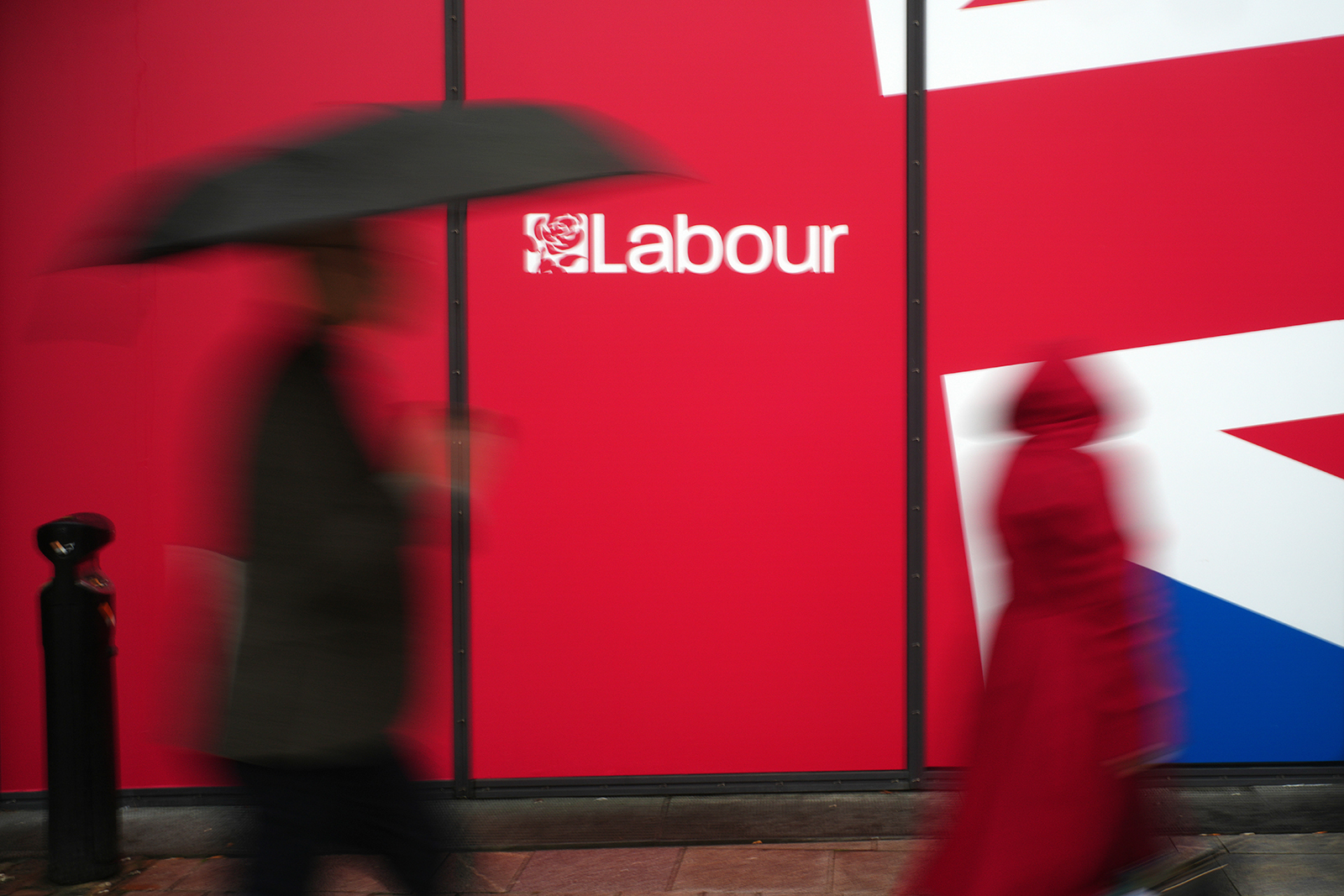 Blurred figures against a red Labour party backdrop