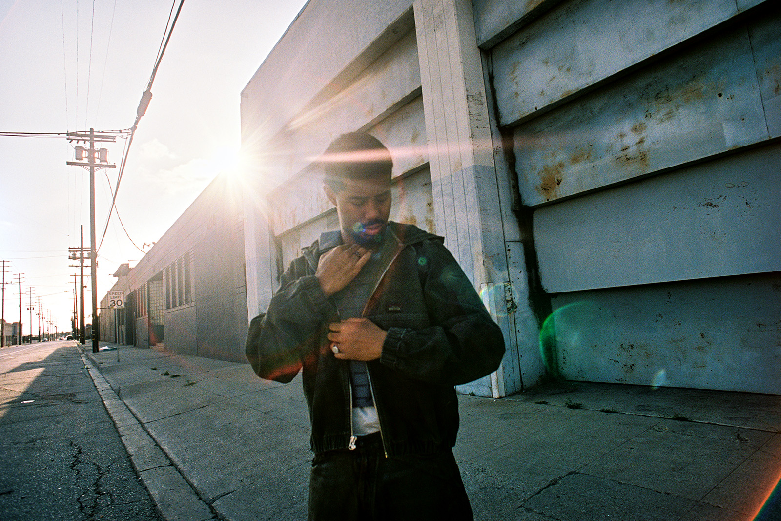 Musician Mustafa looks down at the ground, with the sun shining behind him