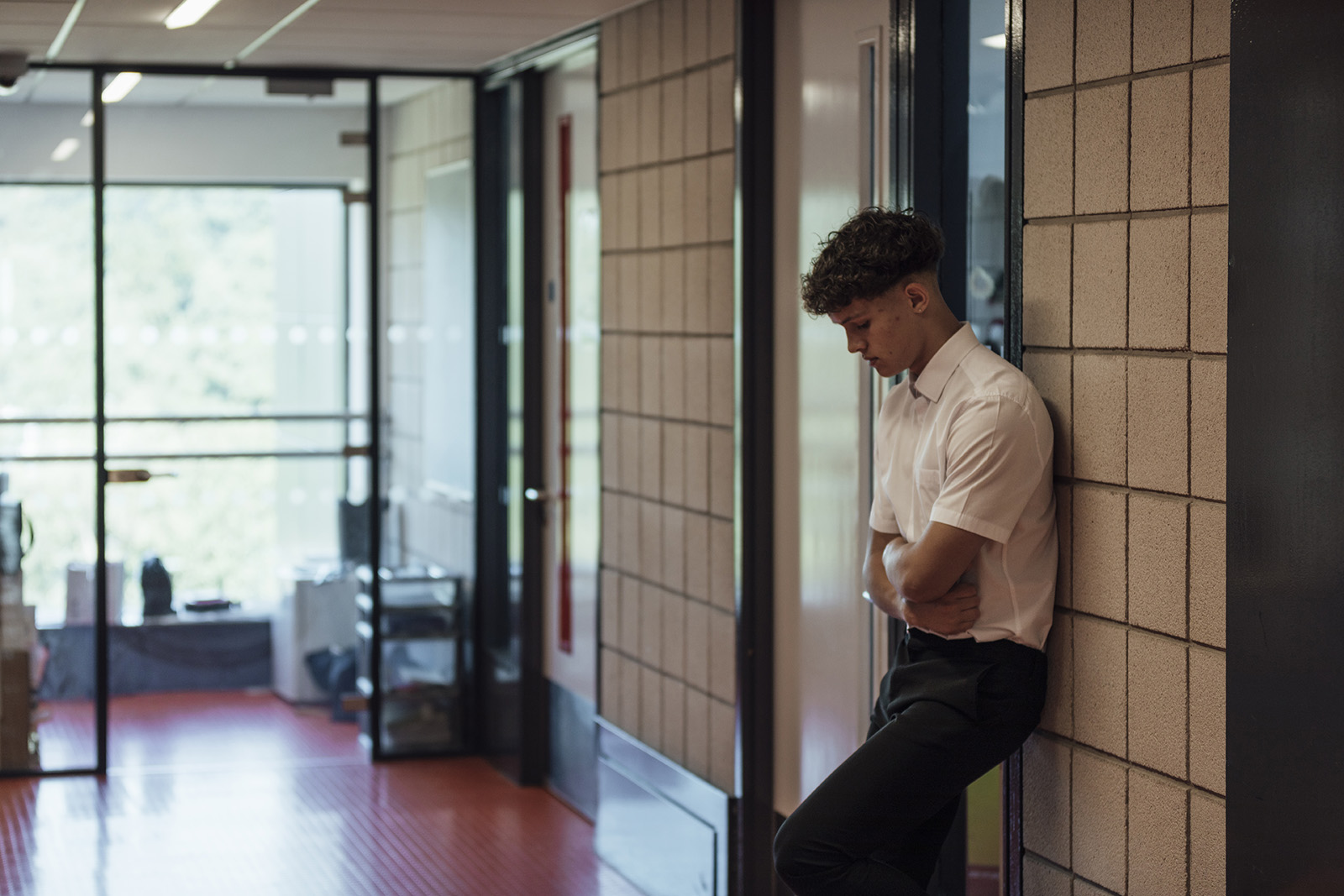 A side view of a young teenage boy who is looking forlorn and sad after being sen out of the classroom in a school in the North East of England. He has his arms folded and is looking down.