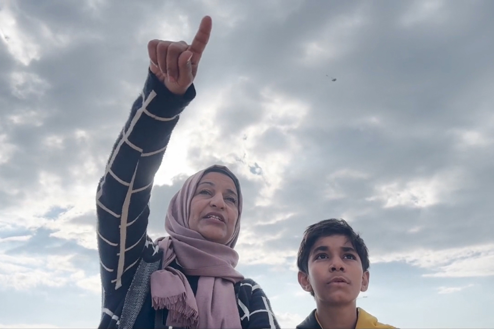 Film still from From Ground Zero of a woman in a head scarf pointing to the sky with a young boy next to hear