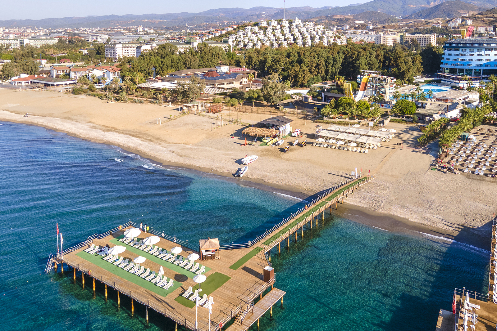 A jetty in the sea at Bera Alanya Resort with white sunbeds and umbrellas.