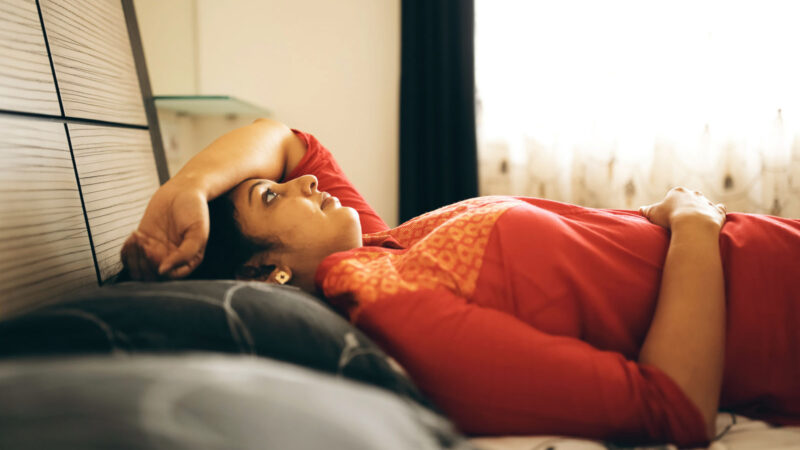 Mature South Asian woman lying on bed with her arm over her head.