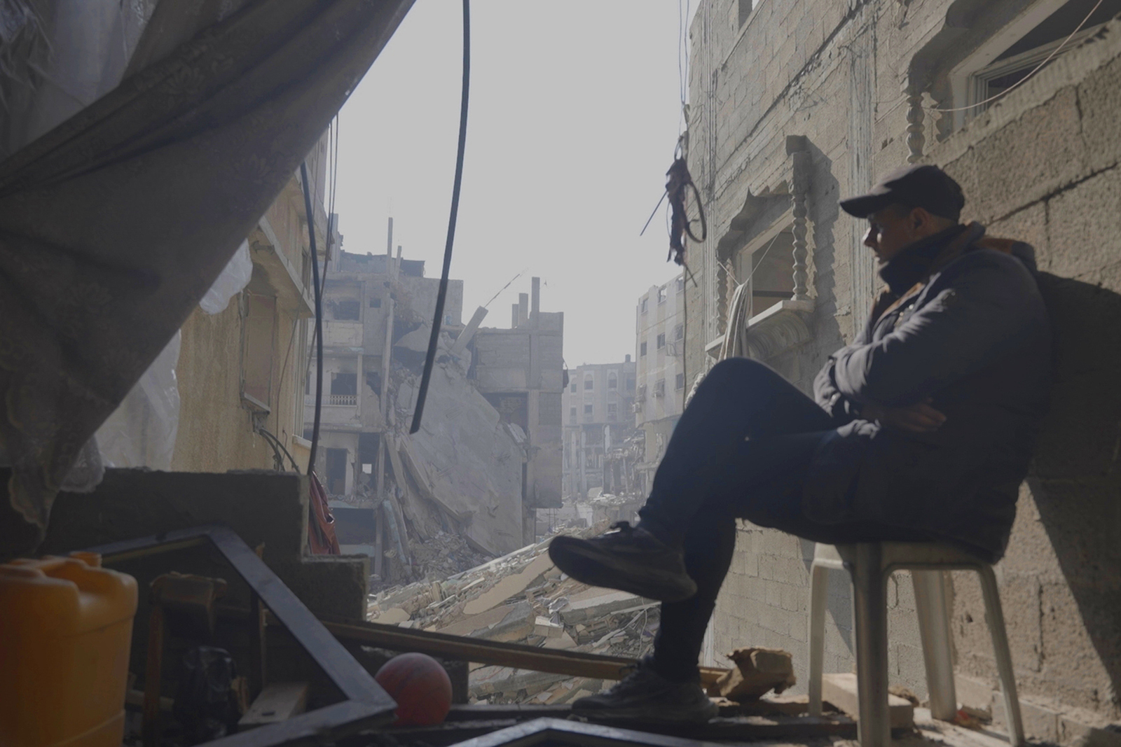 A scene from Sorry Cinema shows a man sitting on a plastic chair amid a destroyed building