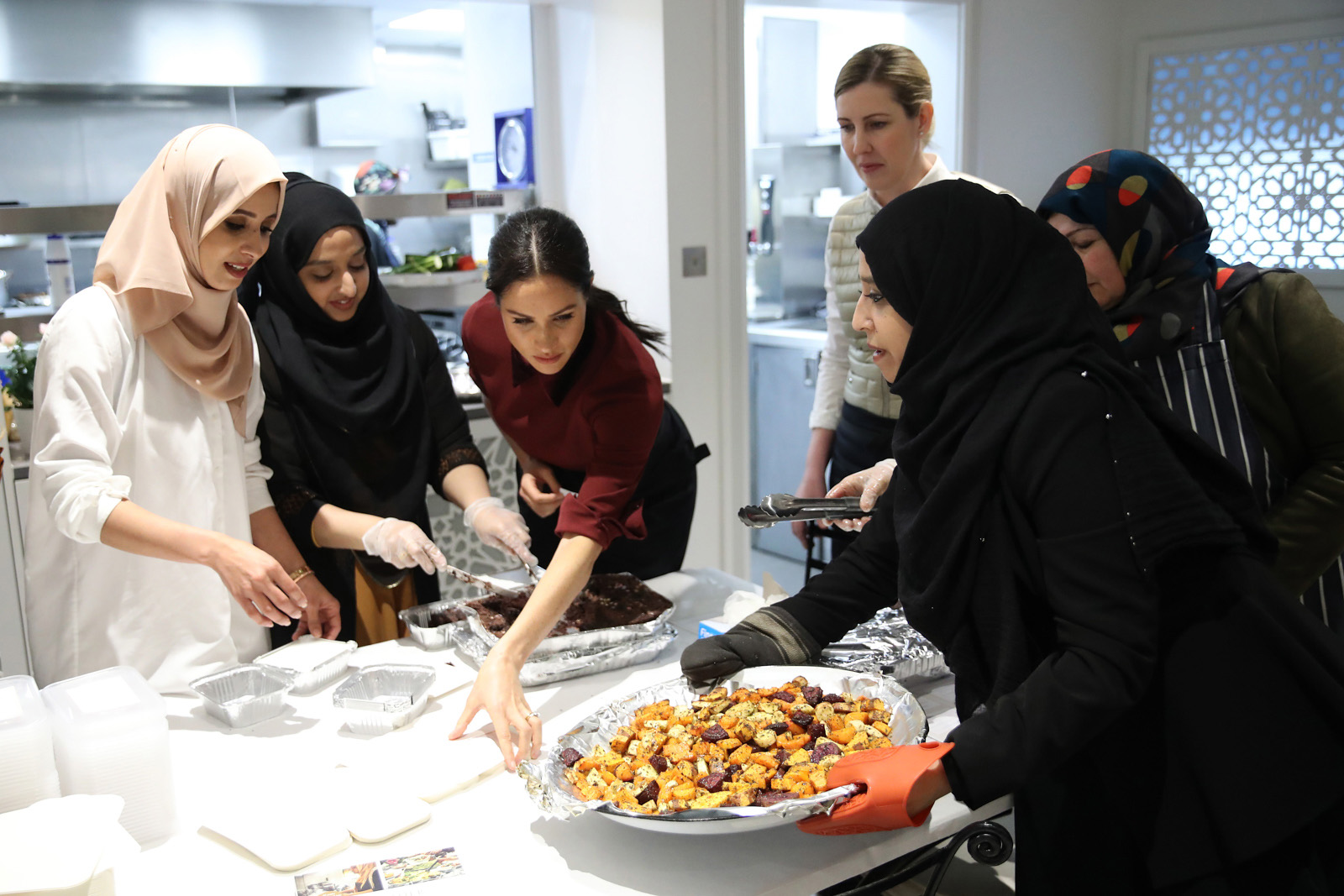 Meghan, Duchess of Sussex(C)  visits the Hubb Community Kitchen in London on November 21, 2018 to celebrate the success of their cookbook. - The kitchen was set up by women affected by the Grenfell tower fire and Meghan, Duchess of Sussex wrote a foreword to the cookbook to help raise funds for the victims. 