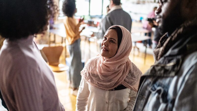 Three people talking, including a women in a headscarf (centre)
