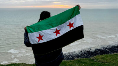 Zahra Albarazi facing away from camera with the Syrian flag held up behind her