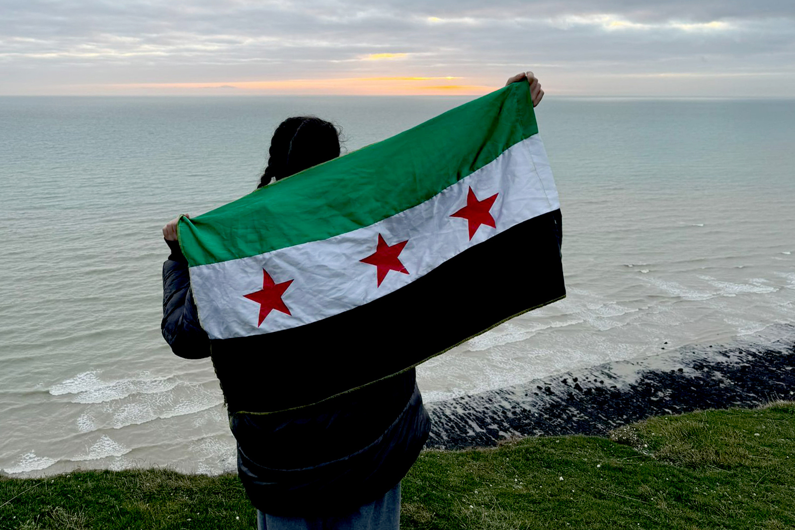 Zahra Albarazi facing away from camera with the Syrian flag held up behind her