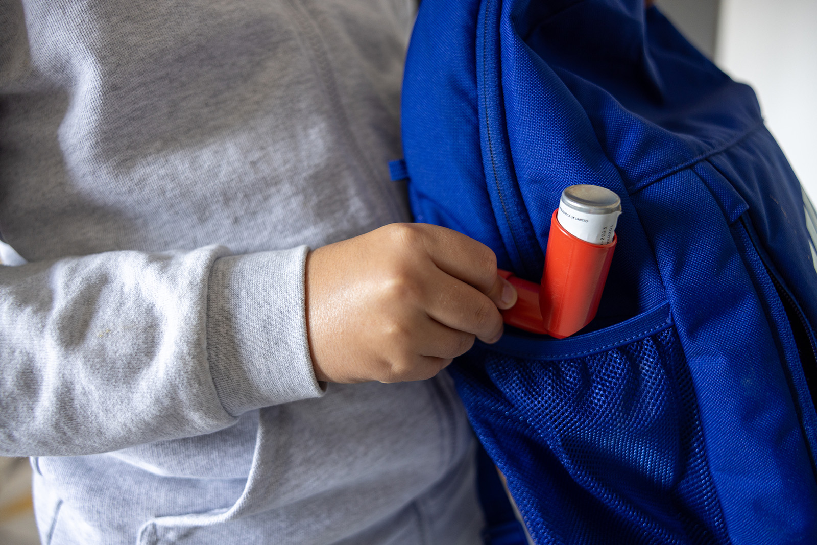 Unrecognizable 11-year-old asthmatic  schoolboy, packing his asthma inhaler into backpack