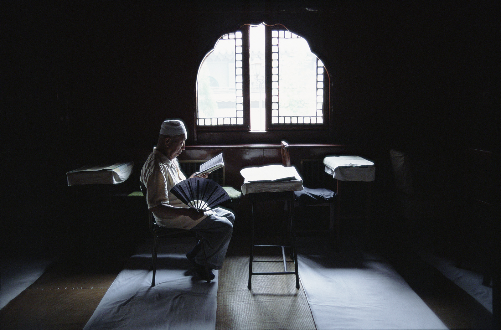 A Muslim man reading the Qur'an by a window in the interior of the Niujie Mosque in Beijing.