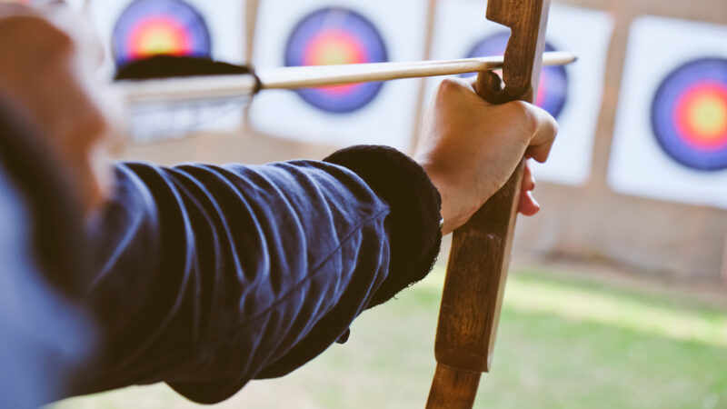 close up image of Archer holds his bow aiming at a target.
