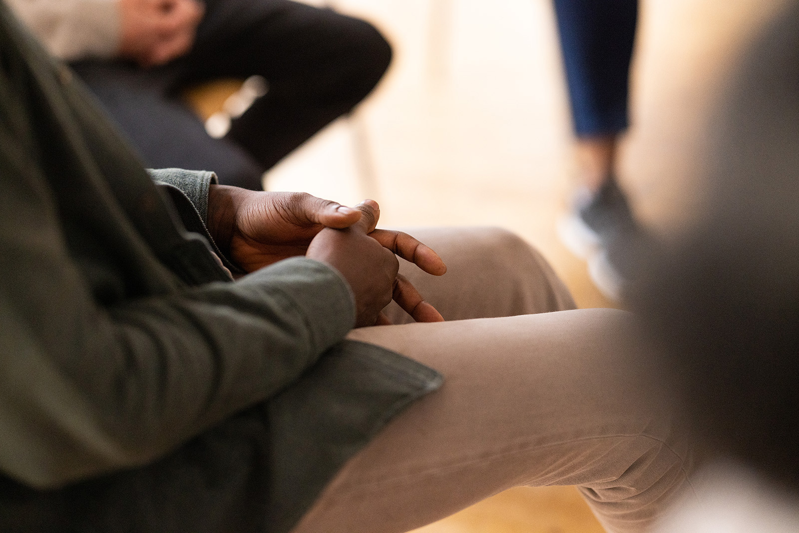 Close-up of a man sitting in a circle during group therapy with his hands clasped. Cropped shot of participants in mental health therapy session.