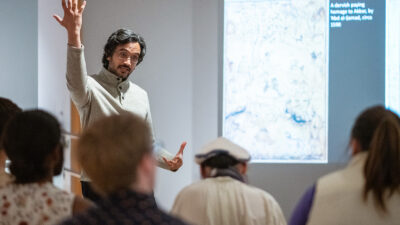 Murad Khan Mumtaz, wearing glasses, gestures while addressing a group of students