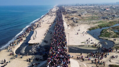 An aerial picture of a road filled with people flanked by the coast on the left and a rubble-strewn landscape on the right