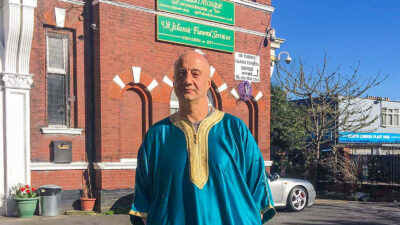 Man in blue robe stands outside mosque