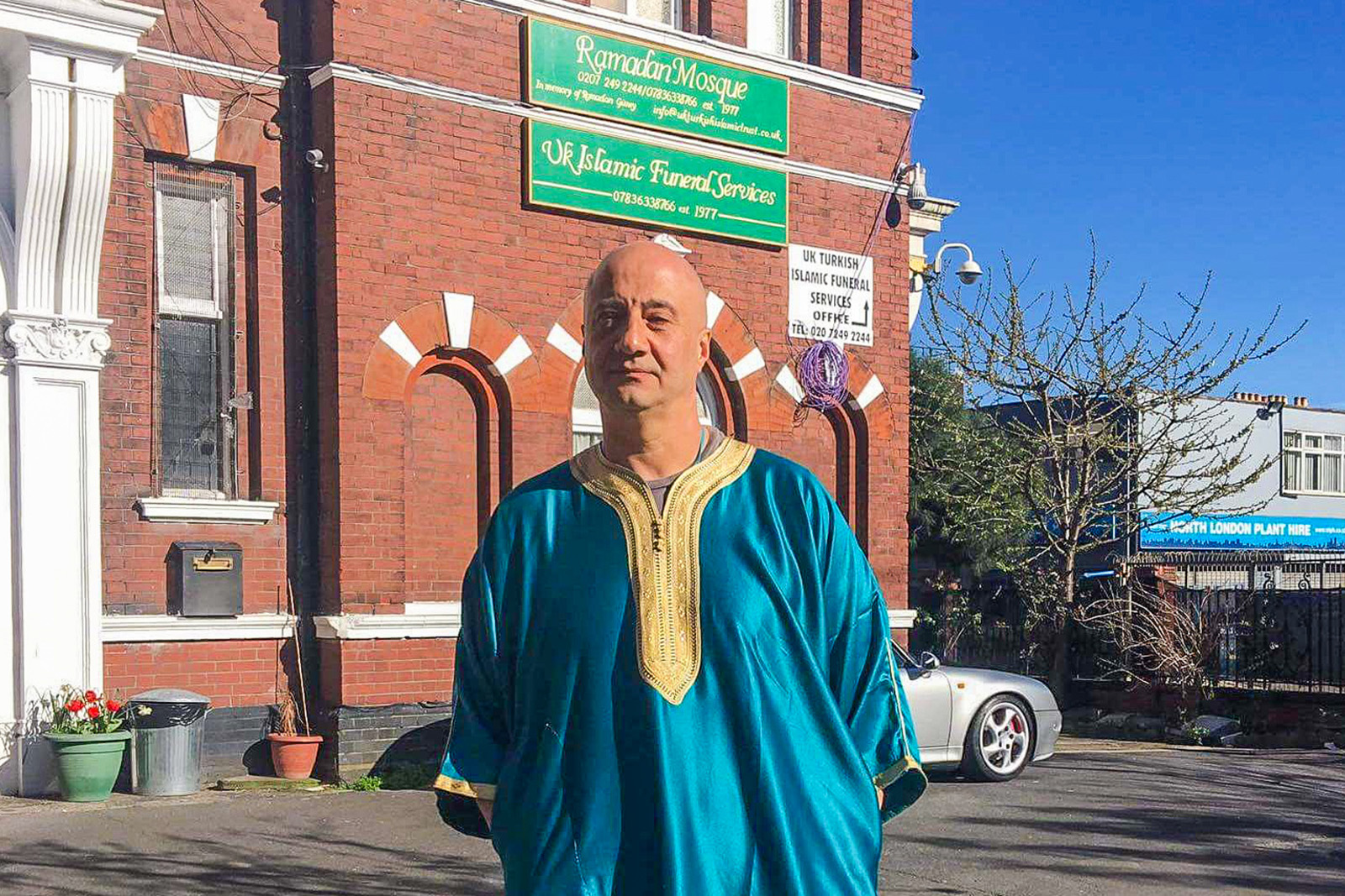 Man in blue robe stands outside mosque