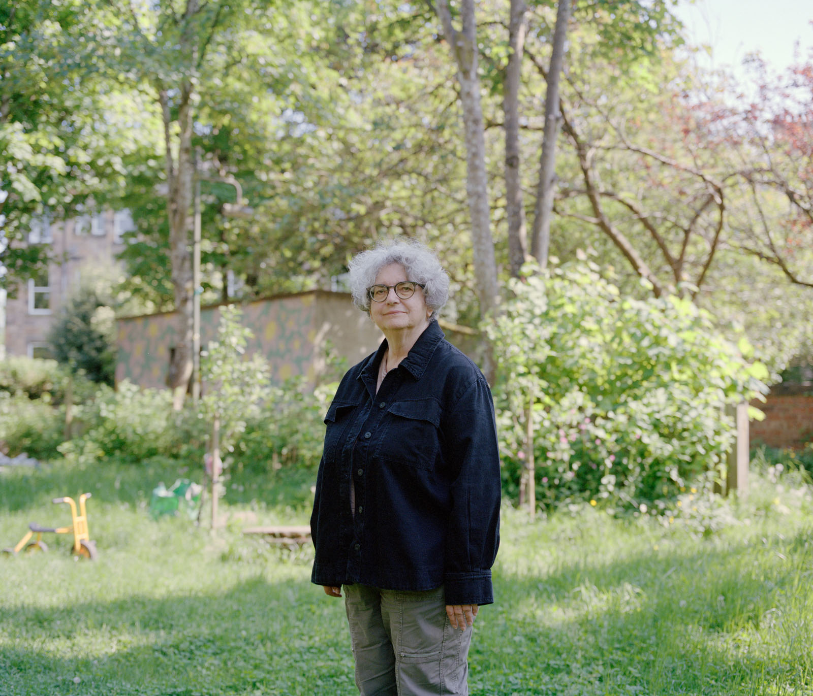 A woman with grey hair and glasses standing in a garden