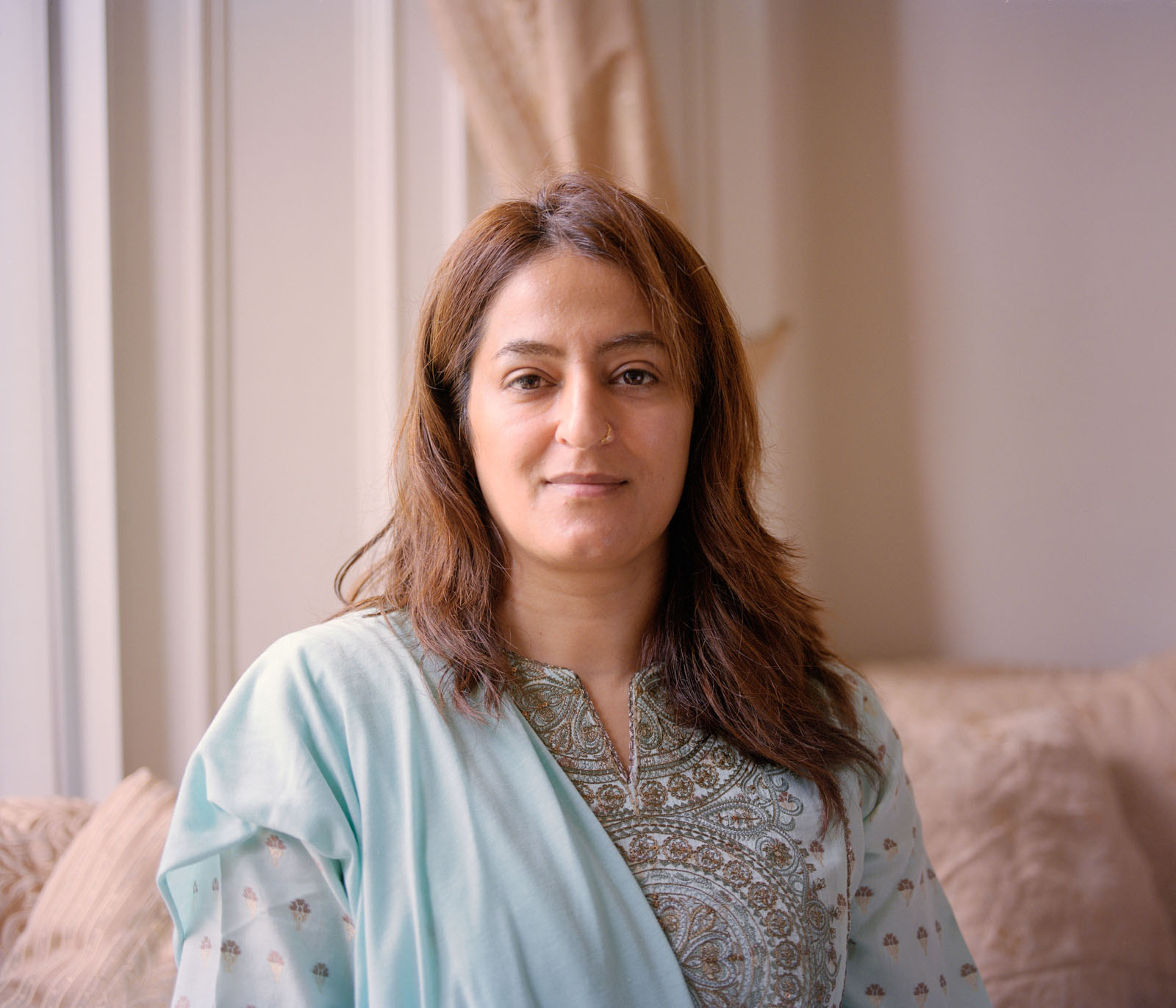 A British Pakistani woman with shoulder length brown hair sitting on a sofa