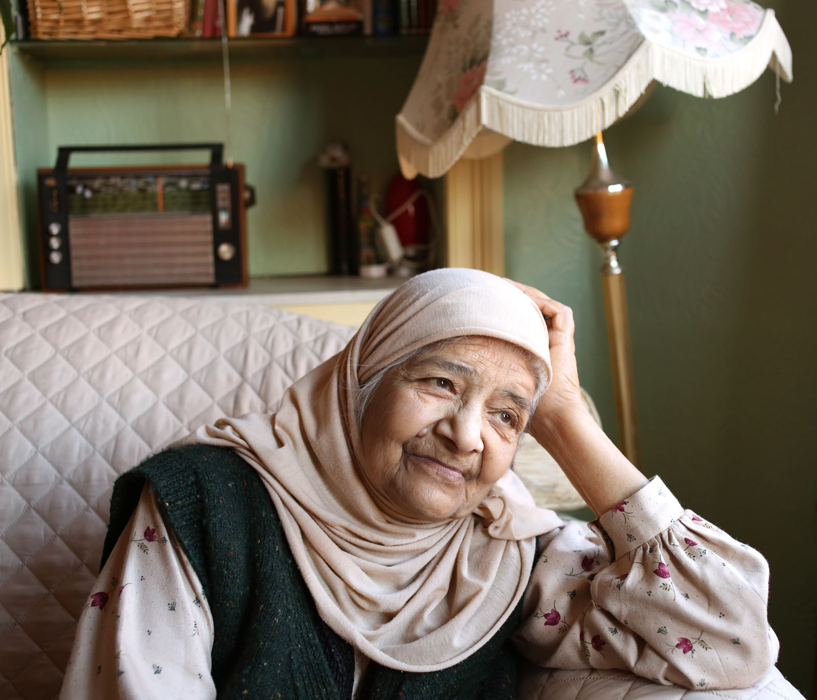 An older British Pakistani Muslim woman pictured at home, resting her head on her hand and looking out a window 