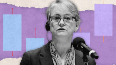 Yvette Cooper in greyscale, wearing glasses, against a purple background showing abstract bars as though in a chart