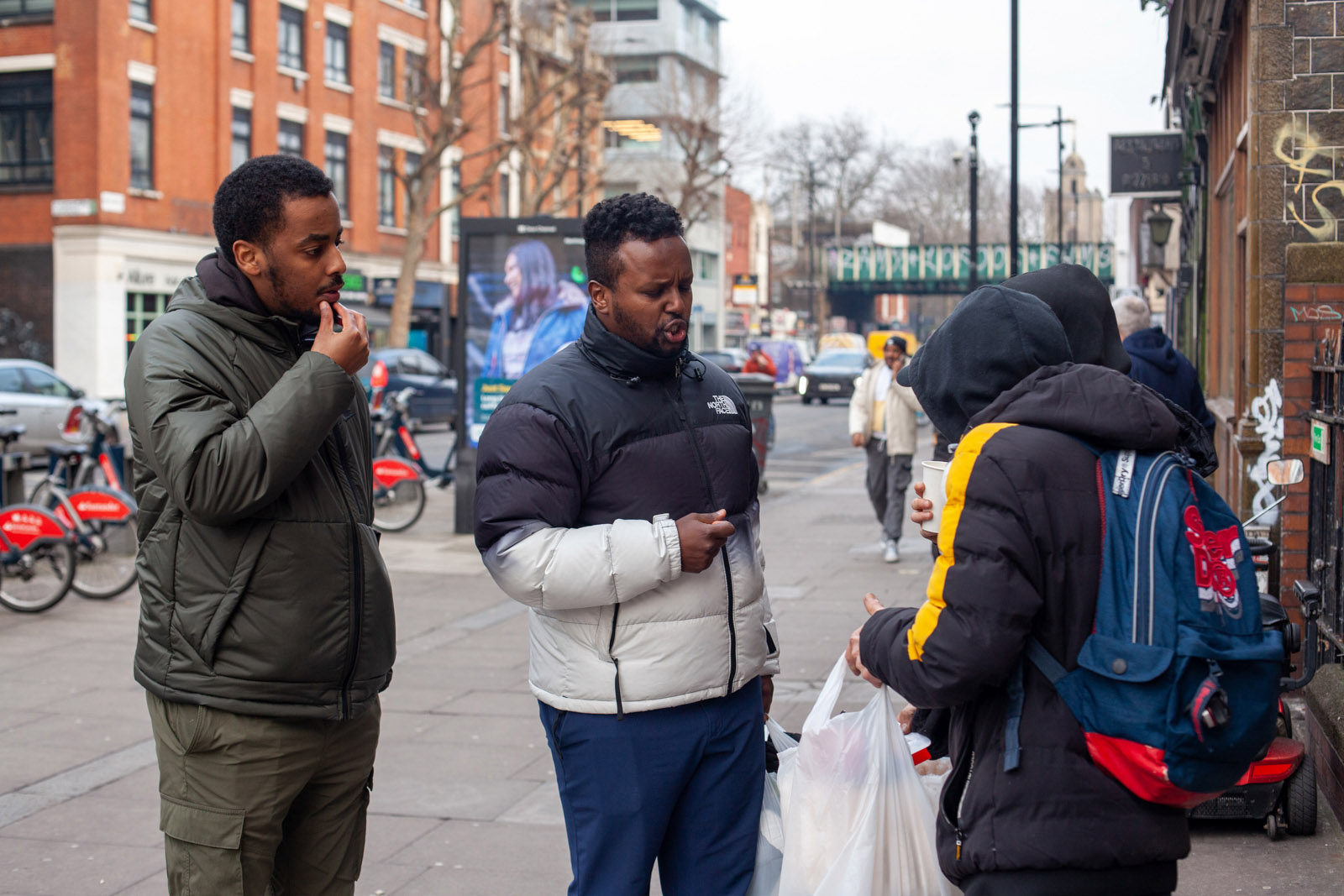 Coffee Afrik outreach workers, Abdirahim Hassan and Mahad Omar, speaking to vulnerable community members in Bethnal Green and handing them free blankets and gloves.