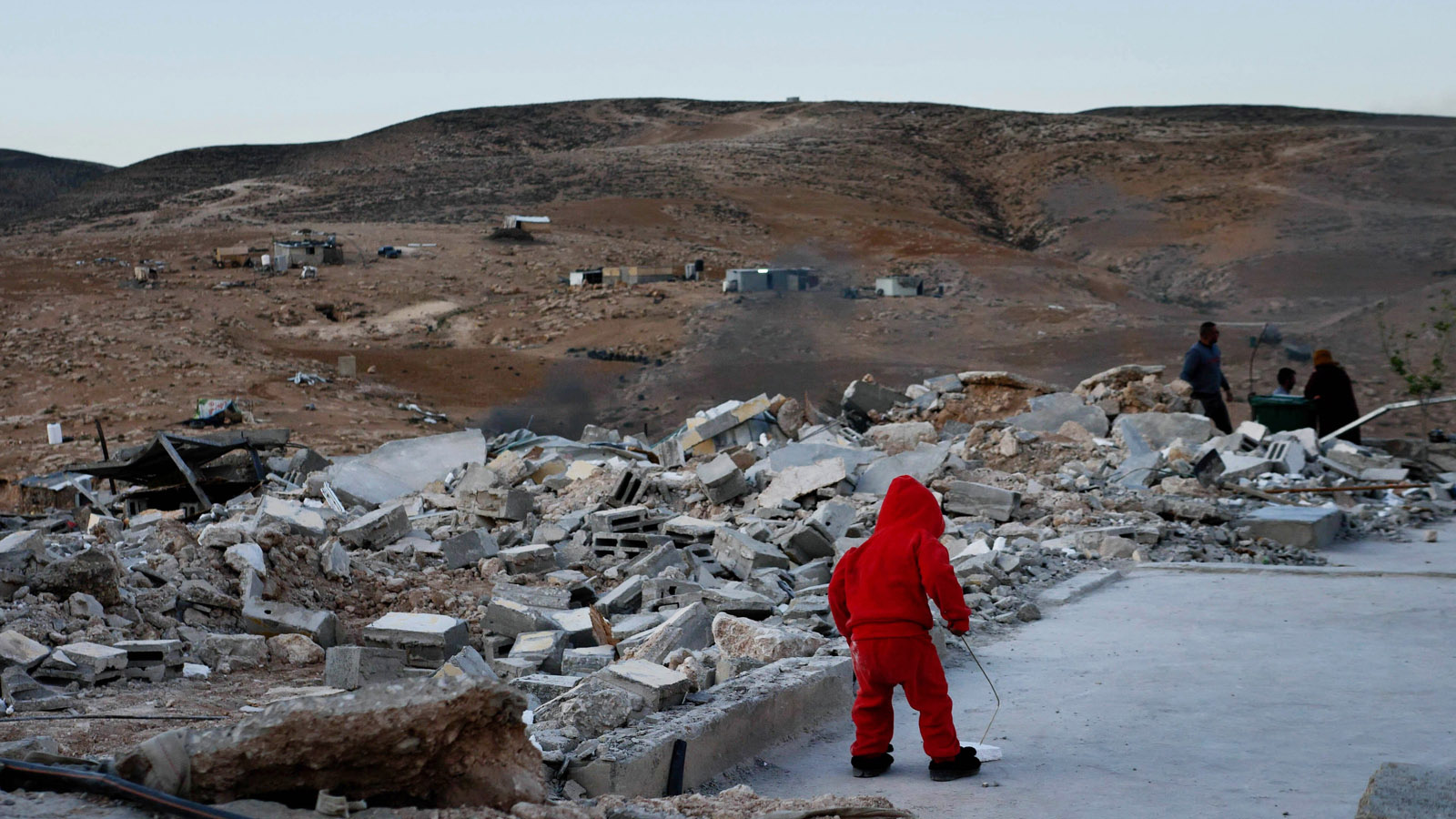 A small child dressed in red stands amid the rubble of a ruined town in a scene from No Other Land